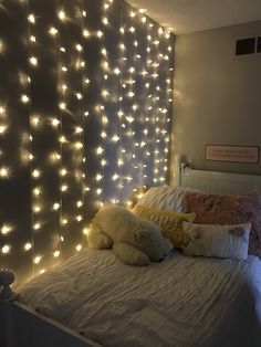 a white bed topped with lots of lights next to a wall covered in string lights