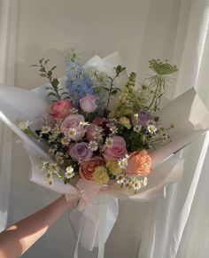 a bouquet of flowers is being held up by someone's hand in front of a window