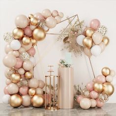 a pink and gold balloon arch on a marble table next to a vase with flowers