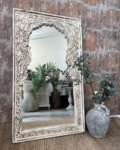 a mirror sitting on top of a table next to a vase filled with plant life