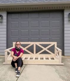 a woman sitting on top of a wooden bench in front of a garage door,