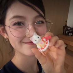 a woman wearing glasses holding up a hello kitty cookie