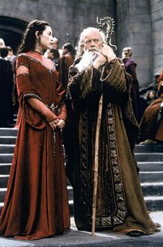 two men dressed in medieval clothing standing next to each other on steps with people watching