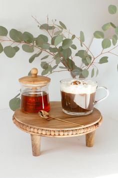 a wooden table topped with a cup of coffee next to a vase filled with leaves