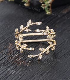 a gold ring with leaves and diamonds on a wooden table next to some flowers,