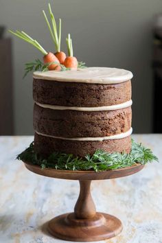 a chocolate cake with frosting and carrots on top sitting on a wooden stand