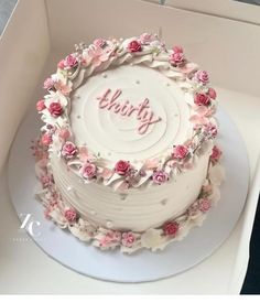 a white cake with pink flowers and the word happy on it in a box that is open