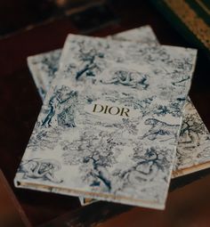 two books sitting on top of a wooden table next to a book with the word dior written on it