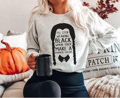 a woman sitting on a couch holding a coffee mug and wearing a sweatshirt that says, i'll stop making black hair when they make darker ends