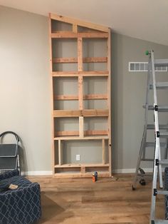 an empty room with two ladders and a bookcase in the corner, next to a chair