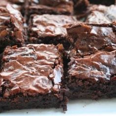 chocolate brownies sitting on top of each other in front of a white plate filled with more brownies