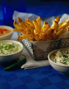 some food is sitting in bowls on a blue tablecloth with silverware and napkins