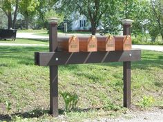 three mailboxes sitting on top of a wooden sign in the grass near trees