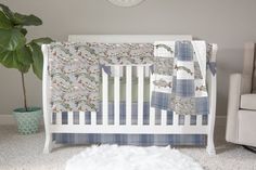 a white crib with blue and green bedding next to a potted plant