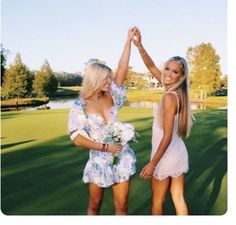 two beautiful young women standing next to each other on top of a lush green field