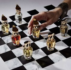 a person is playing chess on a checkerboard with perfume bottles in the background