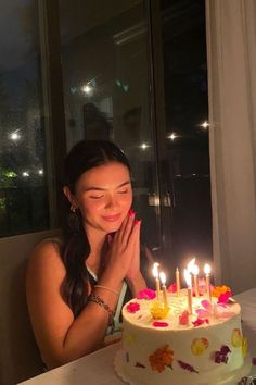 a woman sitting in front of a cake with lit candles