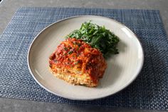 a white plate topped with meat covered in marinara sauce next to a green leafy salad