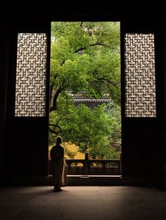 a person standing in front of an open door with trees outside the window at night