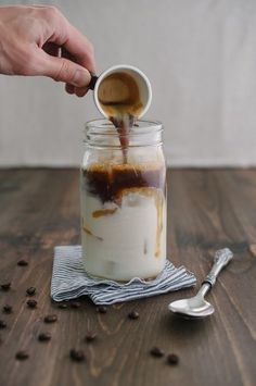 someone pouring coffee into a jar on top of a wooden table