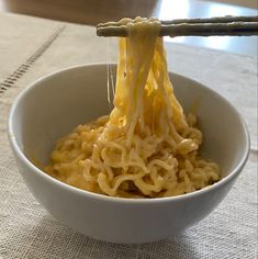 a bowl of noodles is being held up by chopsticks with cheese on top