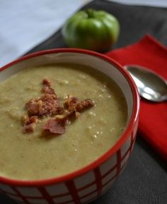 a red and white bowl filled with soup on top of a table next to an apple