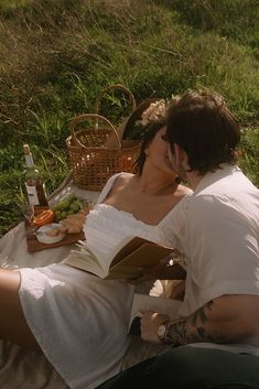 a woman sitting on the ground reading a book and drinking wine in her hand while holding an open book