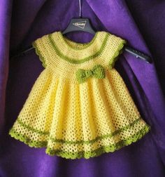 a crocheted yellow dress hanging on a purple cloth