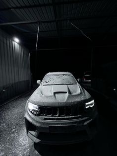 a car is parked in the dark with snow on it's hood and headlights