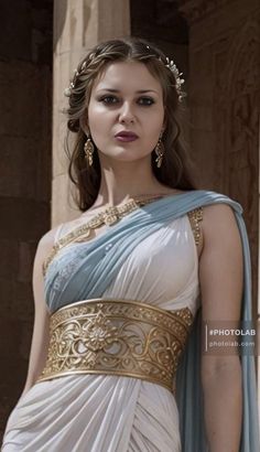 a woman wearing a white and blue dress with gold accents on her head, standing in front of columns