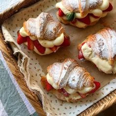 four pastries with strawberries and powdered sugar on them in a wicker basket