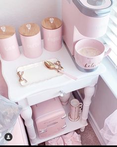 pink kitchen accessories and utensils are arranged on a small white table in front of a window