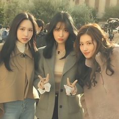 three young women standing next to each other in front of a group of people holding peace signs