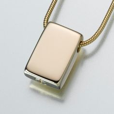 a silver and gold necklace with a square pendant hanging from it's side on a white surface