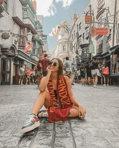 a woman sitting on the ground in front of a street with buildings and people walking around