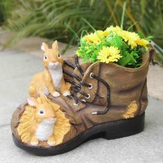 a small toy rabbit sitting on top of a boot next to a planter filled with yellow flowers