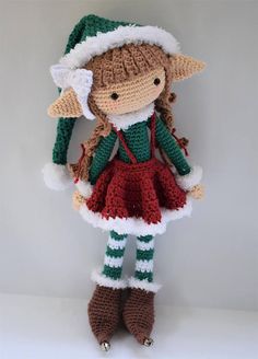 a crocheted doll wearing a green and white hat, red dress, and striped stockings