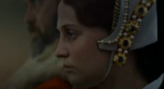 a woman wearing an elaborate head piece with pearls on it's forehead and another man in the background