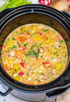 a crock pot filled with chicken and vegetable soup on top of a white table