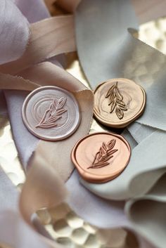 three buttons with leaves on them are sitting on some satin material and one has a ribbon around it