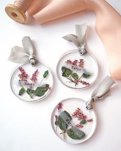 three pendants with flowers and leaves on them sitting next to a thread spool