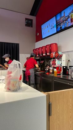 a man standing in front of a counter with food on it and two televisions above him