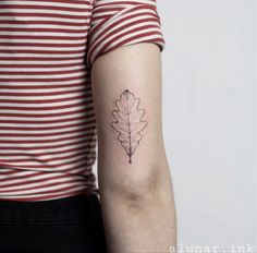 a woman's arm with a single leaf tattoo on the back of her left arm