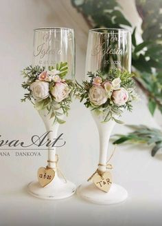 two wine glasses with flowers on them sitting next to each other in front of a plant