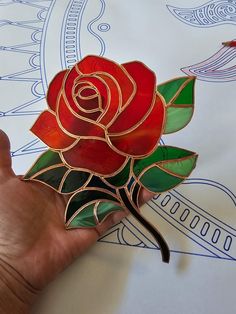 a hand holding a red rose brooch on top of a white sheet with blue and green designs