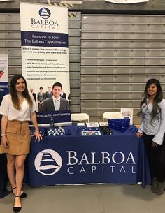 two women standing in front of a table with an advertisement on it that says bailoga capital