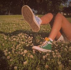 a person sitting in the grass with their feet up and wearing tennis shoes over their ankles