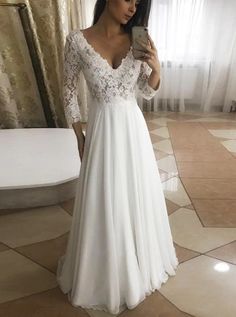 a woman in a white dress taking a selfie with her cell phone while wearing a lace and chiffon wedding gown