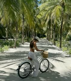 a woman riding a bike down a dirt road next to palm trees