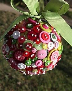 an ornament hanging from a tree decorated with buttons and green ribbon on grass